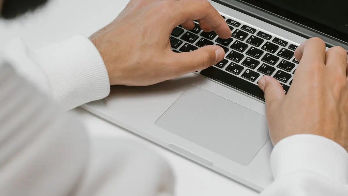 Hands typing on a laptop with code on screen.