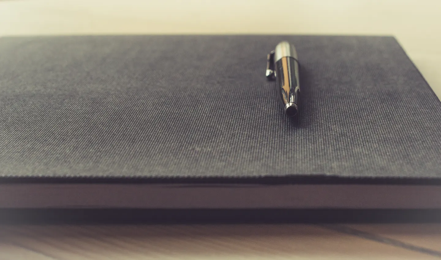 Pen on a black notebook on a wooden table.